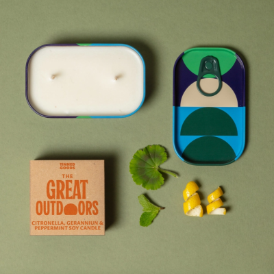 Vela de soja em lata decorada com padrões geométricos, embalagem de cartão e elementos naturais sobre fundo verde