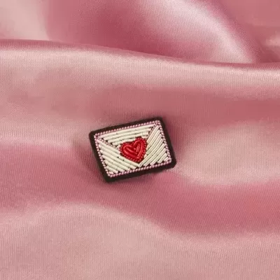 Broche de envelope com coração vermelho sobre tecido de cetim rosa