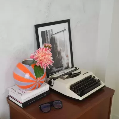 Vaso colorido com flor, máquina de escrever, livros, óculos e fotografia em móvel de madeira