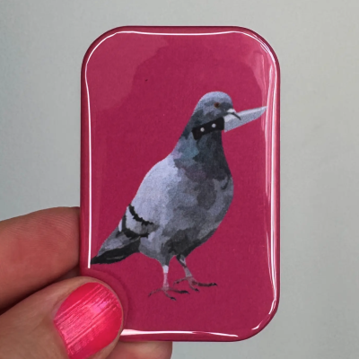 Objeto retangular com ilustração de pombo cinzento com faca numa mão com unha pintada de rosa