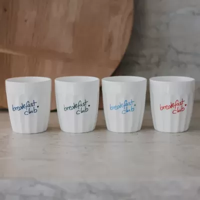 Quatro canecas brancas com texto colorido breakfast club em diferentes cores