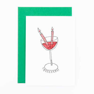 Cartão branco com copo de cocktail, velas acesas e palavra CHEEEEERS, envelope verde