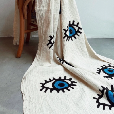 Manta bege com padrão de olhos azuis e pretos sobre cadeira de madeira