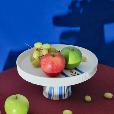 Fruteira cerâmica branca com maçãs vermelhas e verdes e uvas verdes sobre mesa vermelha