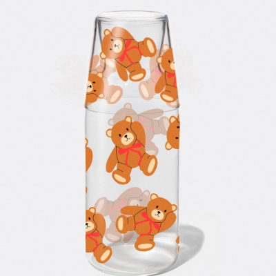 Garrafa de vidro transparente com desenhos de ursinhos castanhos com laços vermelhos.