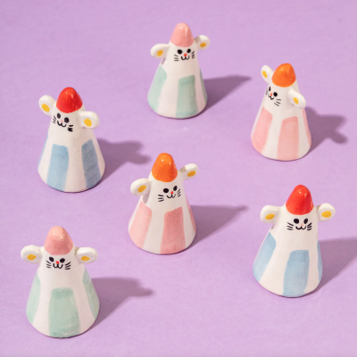 Figuras em cerâmica de ratinho coloridas sobre fundo lilás