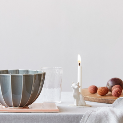 Mesa com taça cinzenta, vela branca em suporte de gato, frutas e vidro transparente