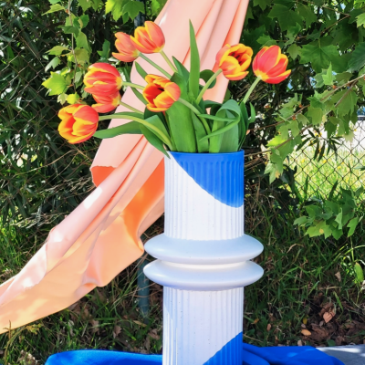 Vaso branco e azul com tulipas num cenário natural e tecido colorido.