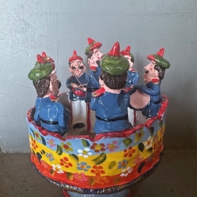 Peça decorativa de cerâmica com seis figuras masculinas em círculo e base floral colorida