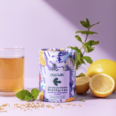 Frasco de infusão Criatura com limões, hortelã e copo de chá sobre fundo lilás