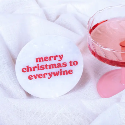 Base redonda de mármore branco com texto vermelho ao lado de um copo rosa com bebida vermelha sobre tecido branco