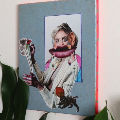 Quadro surrealista colorido pendurado numa parede branca, com planta verde em frente