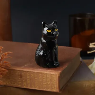 Figurinha preta brilhante de gato com olhos amarelos sobre livro antigo castanho