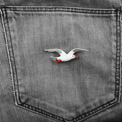 Pino de gaivota branca com detalhes vermelhos num bolso de jeans cinzento.