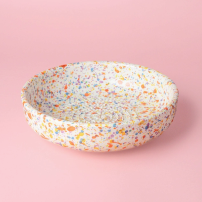 Prato redondo de cerâmica com padrão salpicado colorido sobre fundo rosa