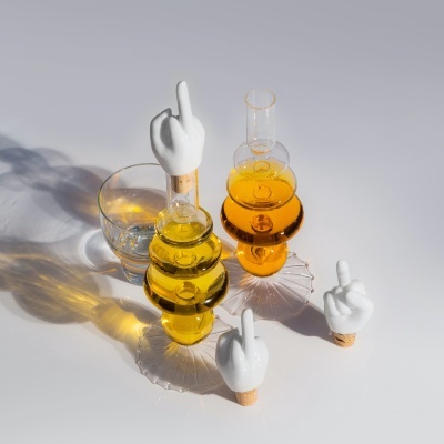 Frascos de vidro com tampas em forma de mão a apontar dedo médio e um copo de vidro