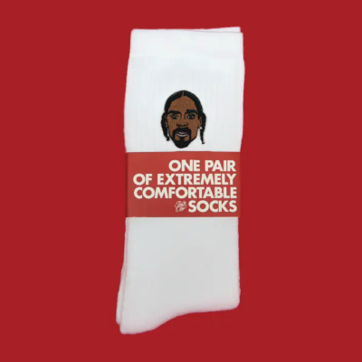 Meias brancas dobradas com bordado de rosto e etiqueta vermelha com texto em branco.