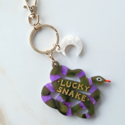 Chaveiro com pendente de cobra verde e roxa com texto dourado e pendente branco em forma de lua