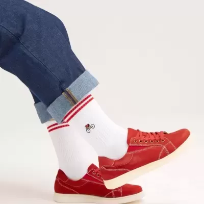 Pés com meias brancas com riscas vermelhas e desenho de bicicleta, calças de ganga e sapatilhas vermelhas