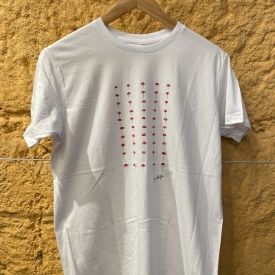 T-shirt branca com padrão de guarda-chuvas vermelhos e assinatura 'By Pipa' contra parede amarela