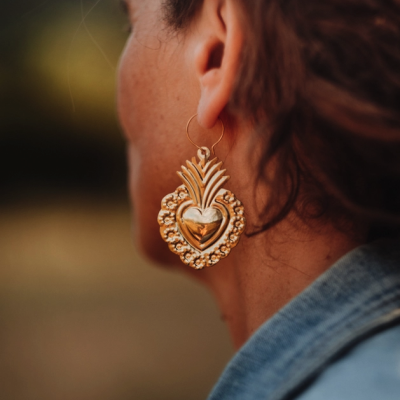 Brinco dourado grande em forma de coração com detalhes ornamentais numa orelha