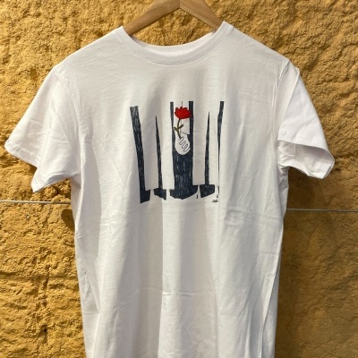 T-shirt branca com estampa de mão segurando flor vermelha pendurada contra parede amarela texturada