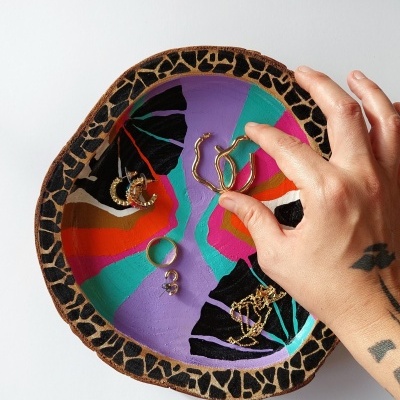 Prato de cerâmica colorido com brincos e uma mão a pegar um brinco