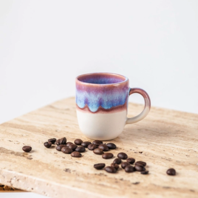 Caneca de cerâmica azul, rosa e branca com grãos de café sobre superfície de pedra