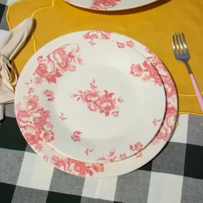 Dois pratos brancos com estampas florais rosa, garfo rosa, guardanapo bege, marcador amarelo e toalha quadriculada verde escuro e branca