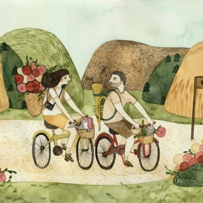 Casal com bicicletas e cestos com gato e flores num caminho entre colinas coloridas