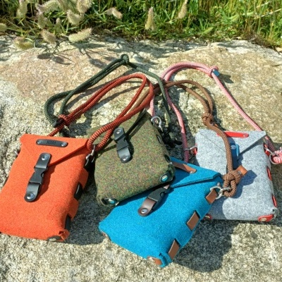 Cinco bolsas pequenas coloridas em tecido felpudo com fechos de pressão e cordões, sobre pedra ao ar livre