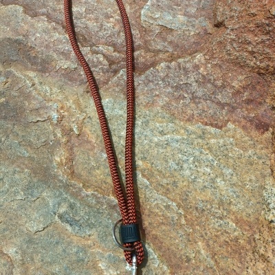 Cordão trançado vermelho e preto com argola metálica sobre pedra