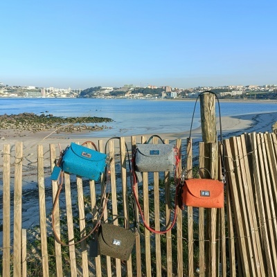 Quatro malas pequenas coloridas penduradas numa vedação de madeira junto à praia