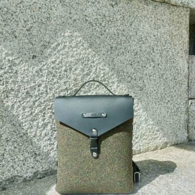 Mochila verde com tampa preta e fecho metálico sobre pedra cinzenta