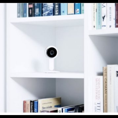 Estante branca com livros e uma câmara de segurança branca no centro.