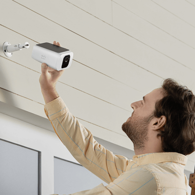 Homem a instalar câmara de segurança branca e preta numa parede de madeira