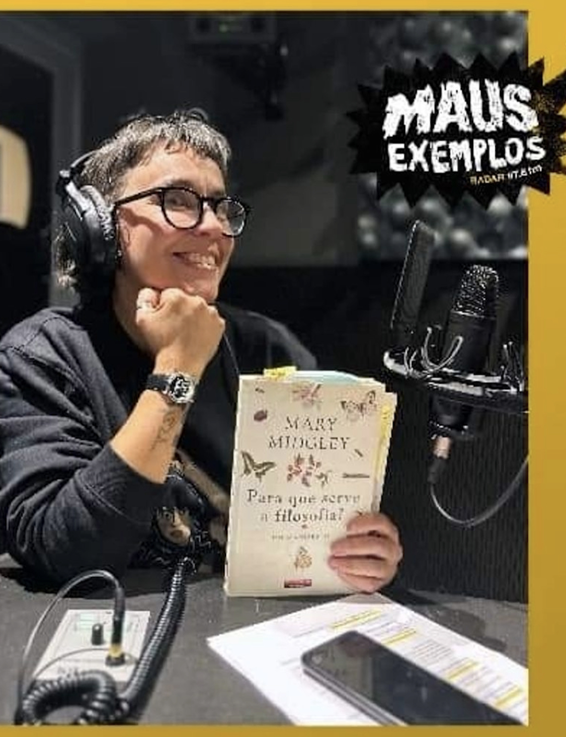 Pessoa com auscultadores segura livro Mary Midgley 'Para que serve a filosofia?' junto a microfone