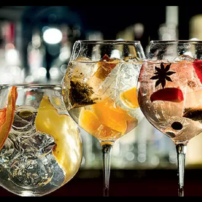 Copos transparentes com drinks variados decorados com frutas e ervas num bar