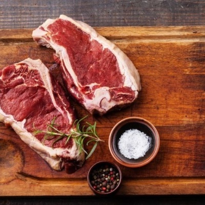 Dois bifes crus numa tábua de madeira com temperos