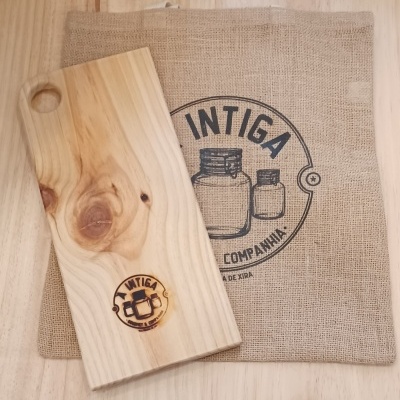 Tábua de madeira clara com logótipo ao lado de uma parede de juta com impressão preta e superfície de madeira.