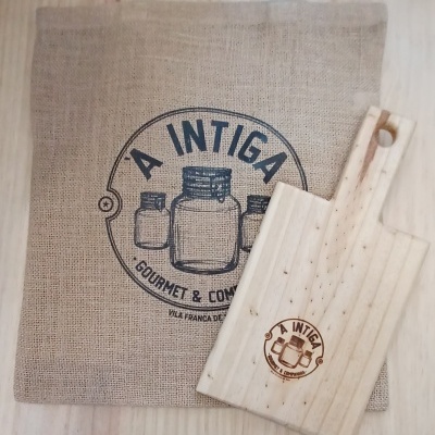 Saco de tecido cor de linho com logotipo preto e tábua de madeira clara com logotipo gravado