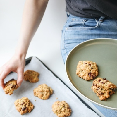 Bolachas de aveia com chocolate em tabuleiro e prato verde, mão a apanhar bolacha.