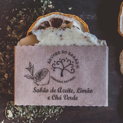 Sabonete natural embalado em papel castanho com texto em português, rodeado por folhas e fatias secas de limão.