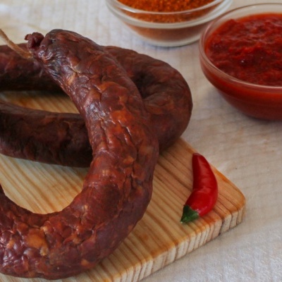 Enchidos escuros numa tábua de madeira com malagueta e tigelas de especiarias e molho