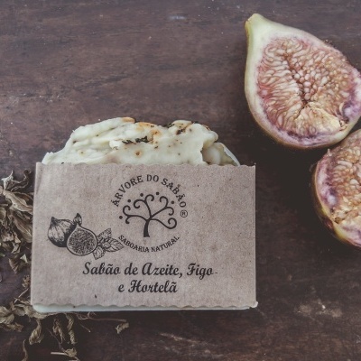 Sabonete artesanal com embalagem em papel reciclado e figos cortados junto, sobre mesa de madeira