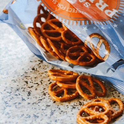 Pacote aberto de pretzels salgados com pretzels fora do pacote sobre superfície de pedra.
