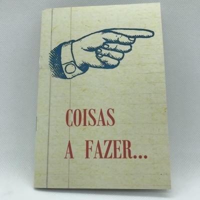 Caderno com capa amarelada com ilustração de mão e texto 'COISAS A FAZER...'