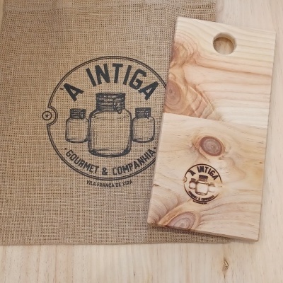 Tábua de madeira clara com buraco redondo e embalagem de juta com logótipo preto A INTIGA