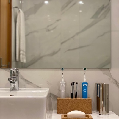 Lavatório branco com escovas de dentes elétricas em suporte de cortiça, pincéis de maquilhagem e sabonete num suporte da marca THE CORKMAN