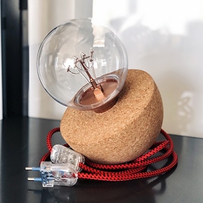 Candeeiro de mesa com base de cortiça e lâmpada de filamento de vidro transparente com cabo vermelho padrão preto.